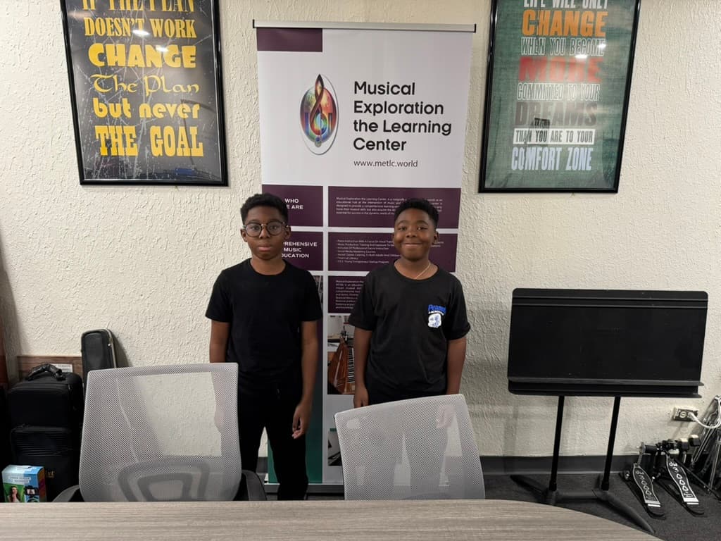 Two METLC students standing in front of the Musical Exploration banner.